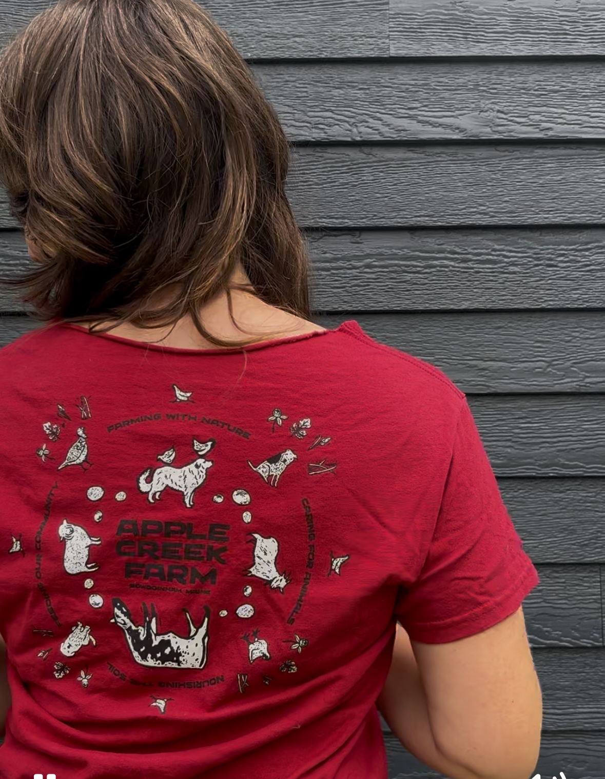 Person wearing a red t-shirt with a circle logo against gray wall.