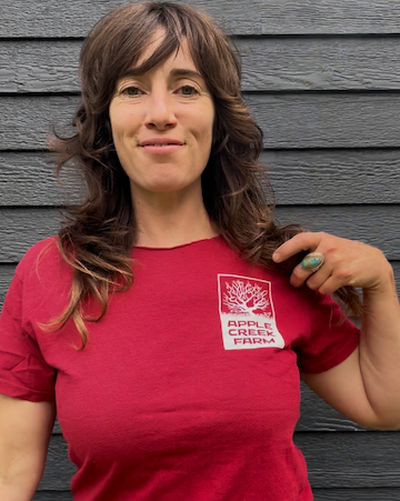 Woman wearing a red t-shirt with a logo against a gray wooden wall
